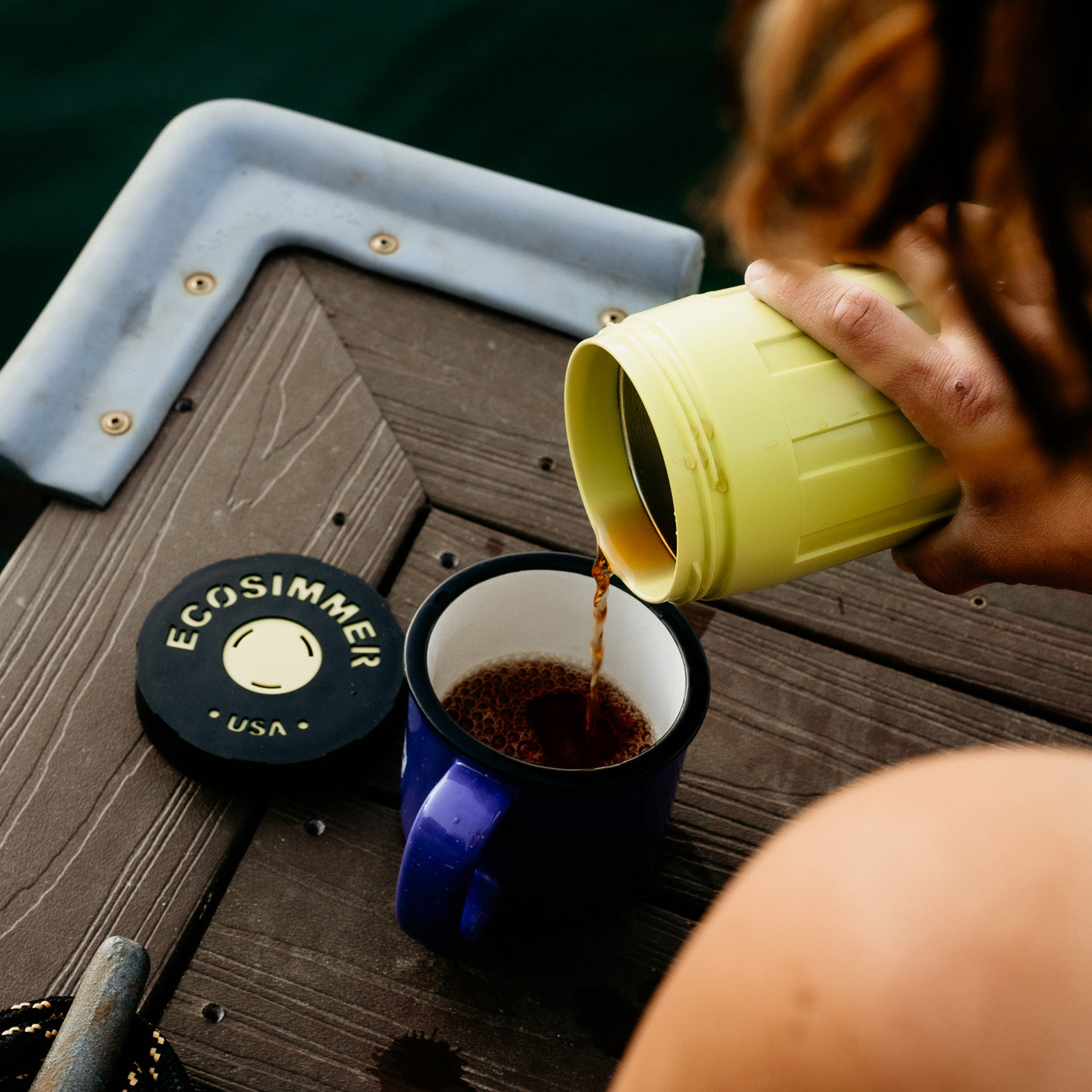Woman pouring hot coffee out of EcoSimmer electric backpacking stove on dock