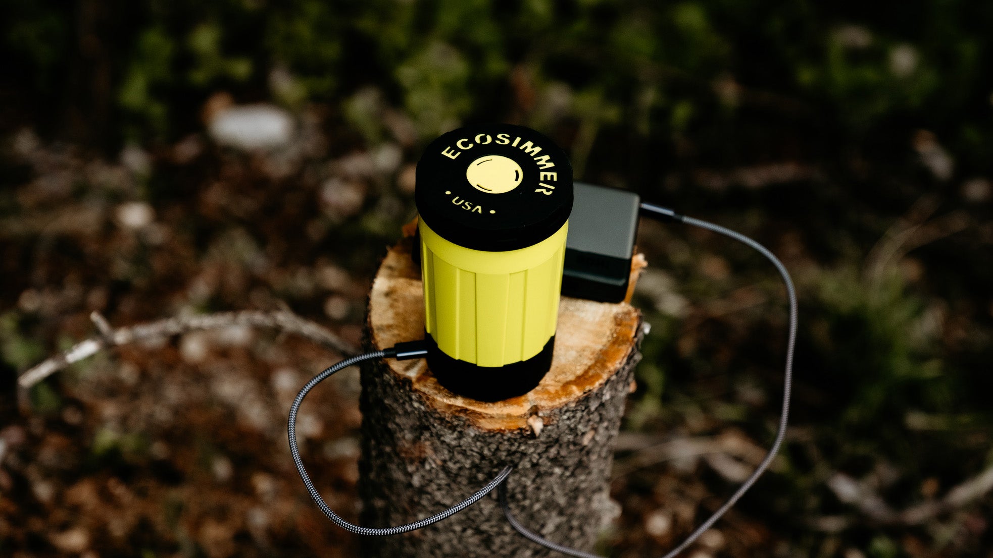 Electric backpacking and camping stove plugged into USB-C battery on tree stump