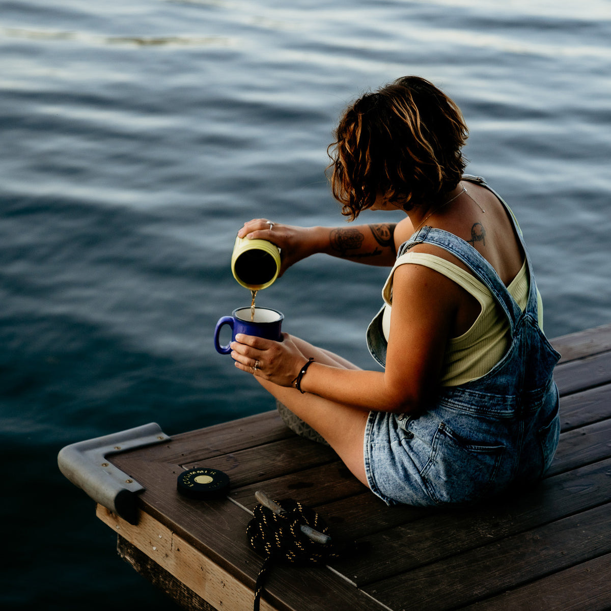 Woman on dock pours coffee made in electric camping stove