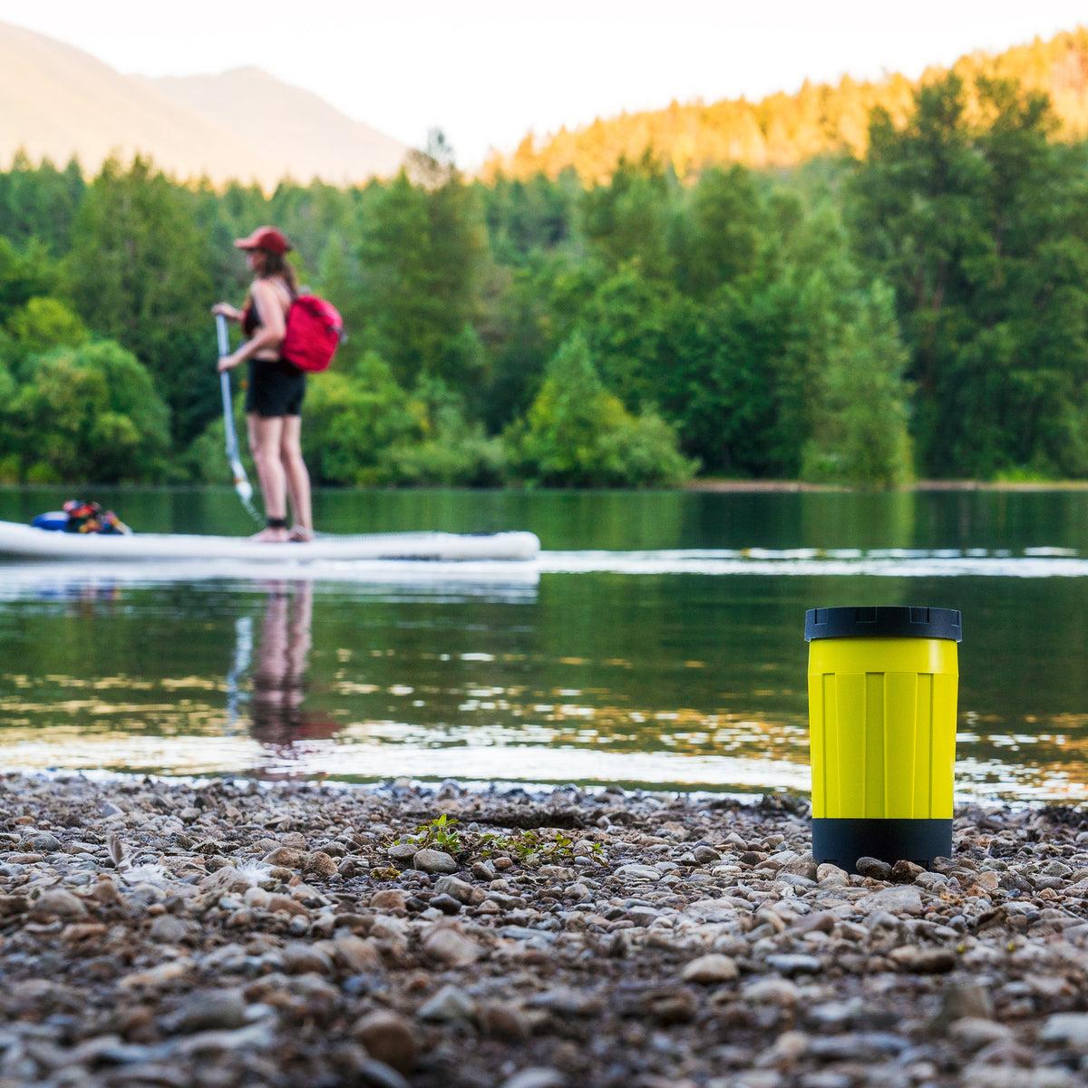 Woman paddle boarding at alpine lake with electric camping stove on shore