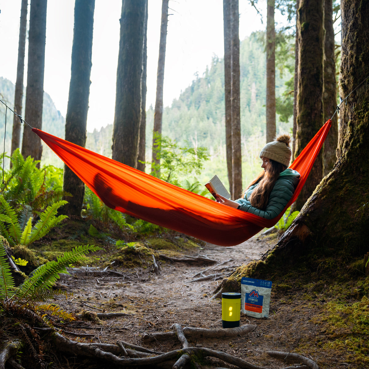 Woman reading in hammock in woods while electric camping stove cooks dinner
